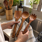 Hands holding acacia wood slotted spoon, skimmer and spatula in a kitchen